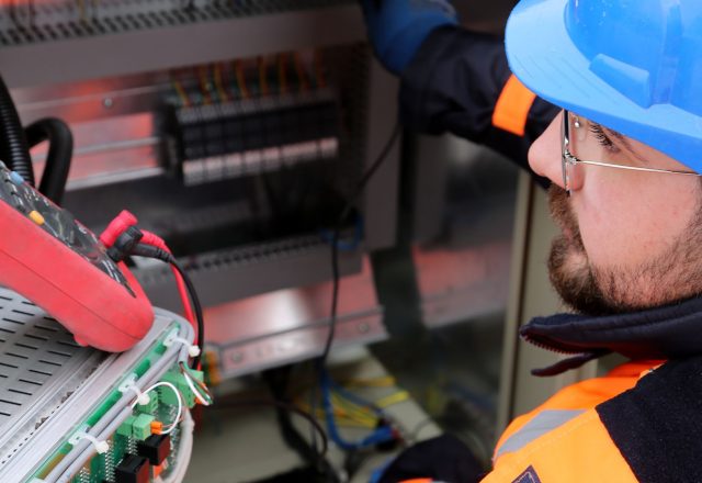 Electrician in hard hat and high-visibility vest working on site electrical equipment