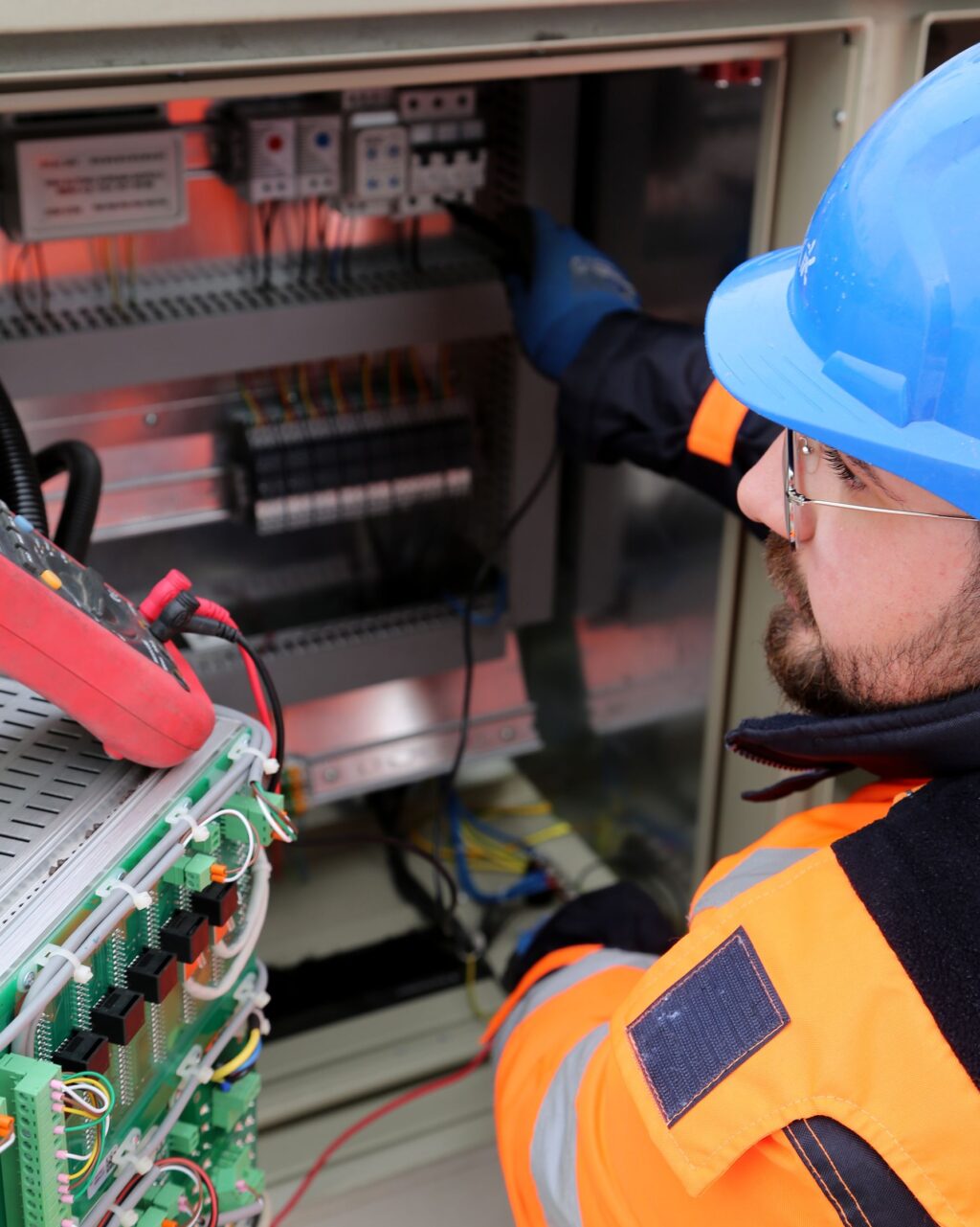 Electrician in hard hat and high-visibility vest working on site electrical equipment